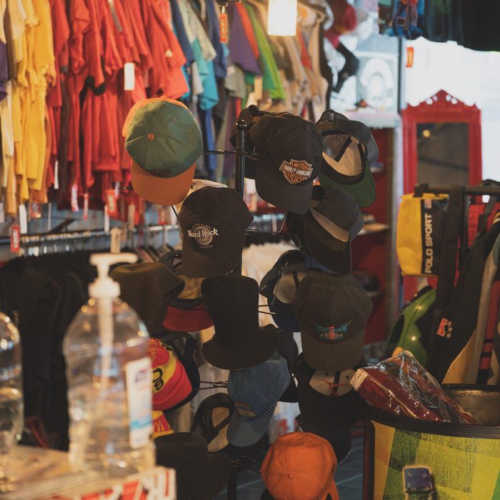 Hat tree stacked with snapbacks in front of a rack of colorful vintage tees