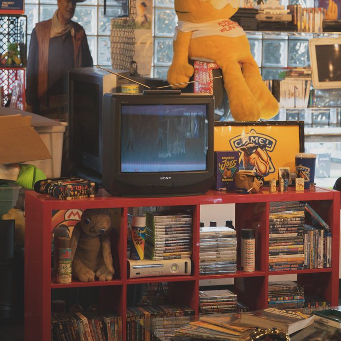 Sony CRT TV and a Garfield plush on a red shelf full of DVDs and games