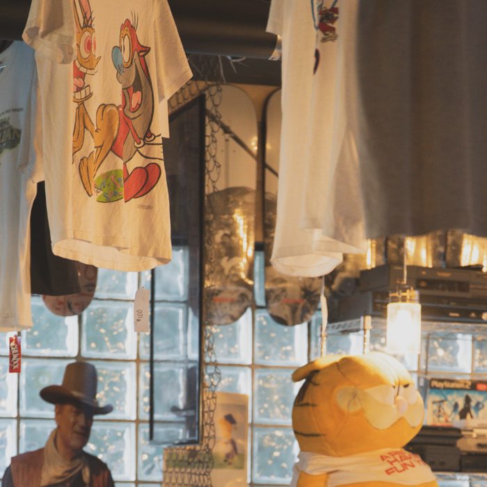 Cartoon graphic tees hanging by the glass-block window next to a John Wayne cutout